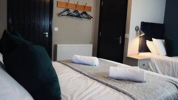 A hotel room with two beds, a coat rack, a door, and a bedside lamp.