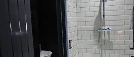 A bathroom with a glass-enclosed shower, white tiled walls, a sink, and a marble floor.