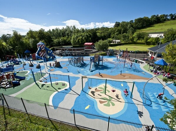 A playground with various play structures, a fenced area, and a building in the background.