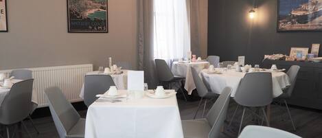 Un restaurante con mesas preparadas para comer, vista al mar y un cartel en la pared.