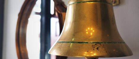 A brass bell mounted on a wall with a rope hanging from its bottom.