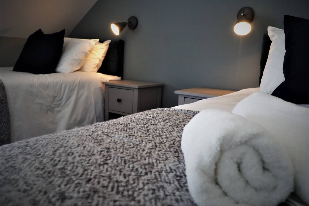 A hotel room with two beds, each with a pillow and a nightstand.
