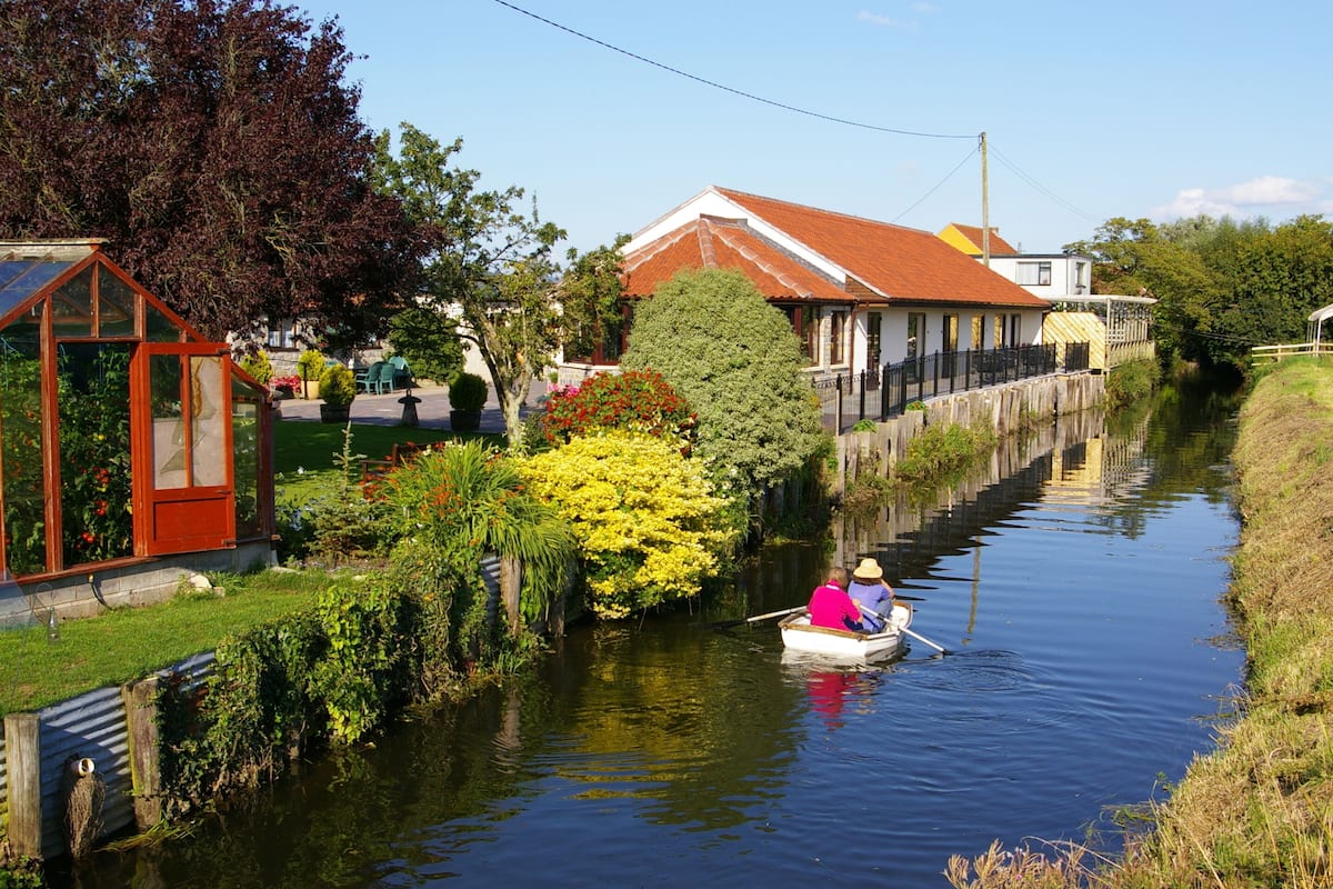 A narrow canal with a row of houses on one side and a greenhouse on the other.