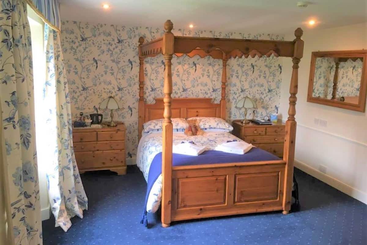 A four-poster bed with a wooden frame, a dresser with drawers, a nightstand, and a mirror on the wall.