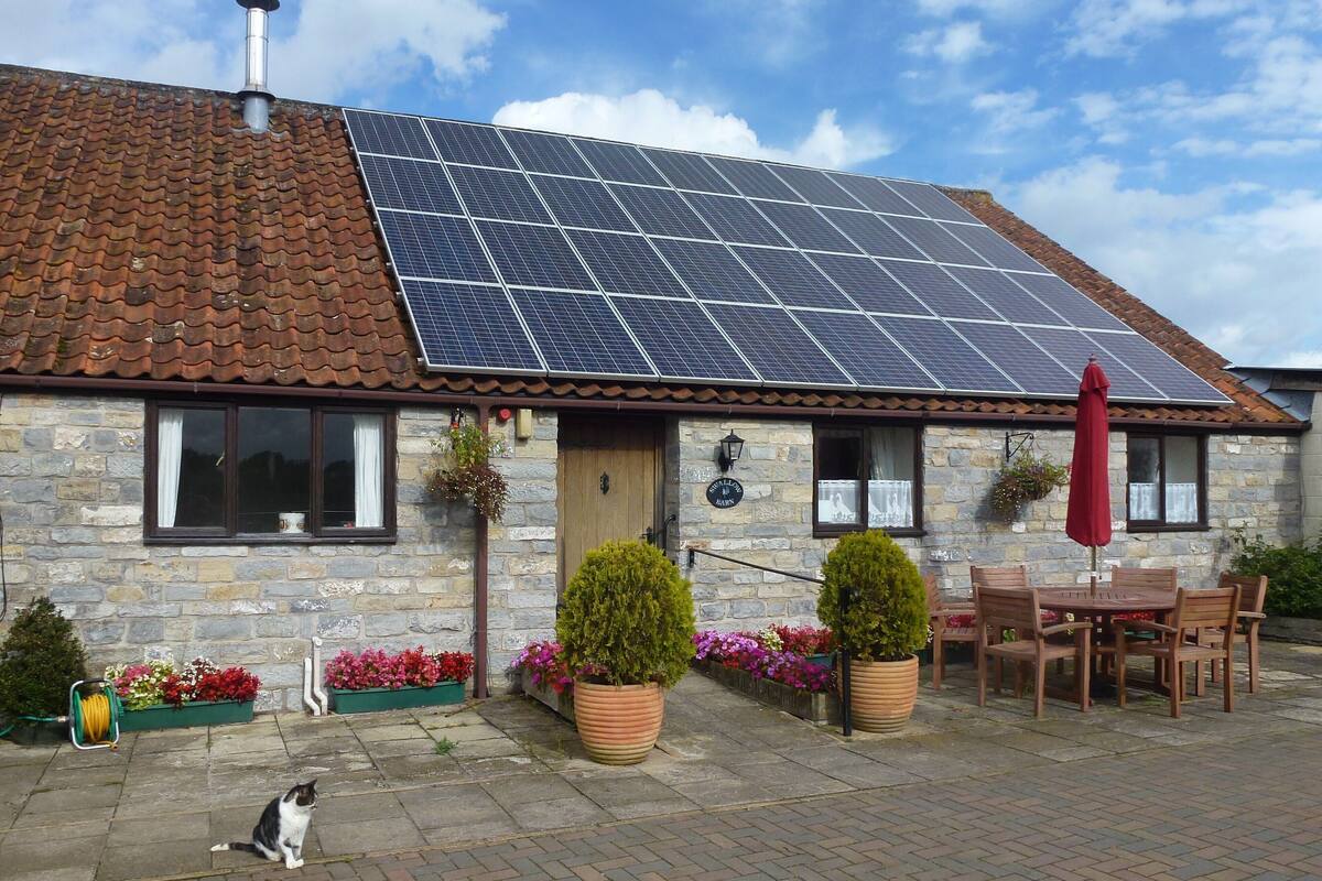 A stone building with a tiled roof, solar panels, a red umbrella, and outdoor seating.