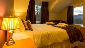 A hotel room with a large bed, a bedside lamp, and a view of mountains through the window. - Craglands Guest House (Keswick)