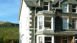 A two-story building with a stone facade, a bay window, and a front porch with a bench. - Craglands Guest House (Keswick)