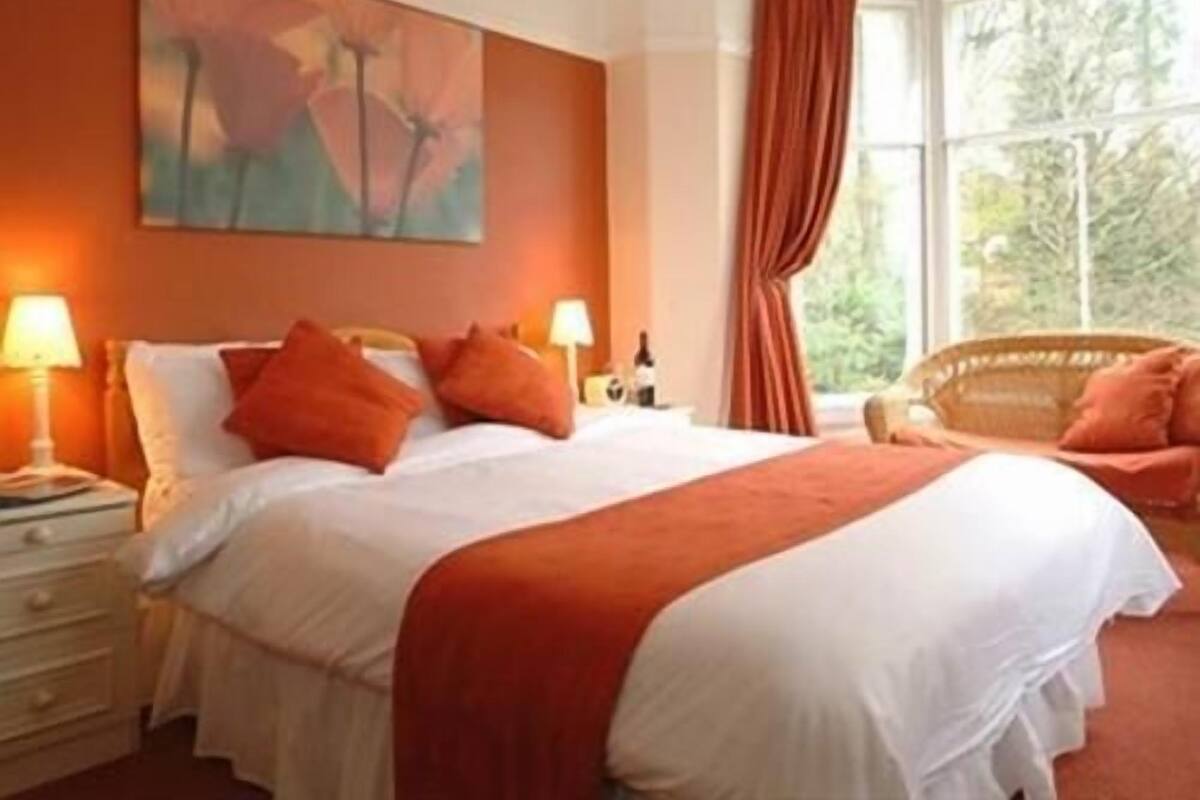 A hotel room with a large bed, two bedside tables with lamps, a window with curtains, and a painting on the wall.