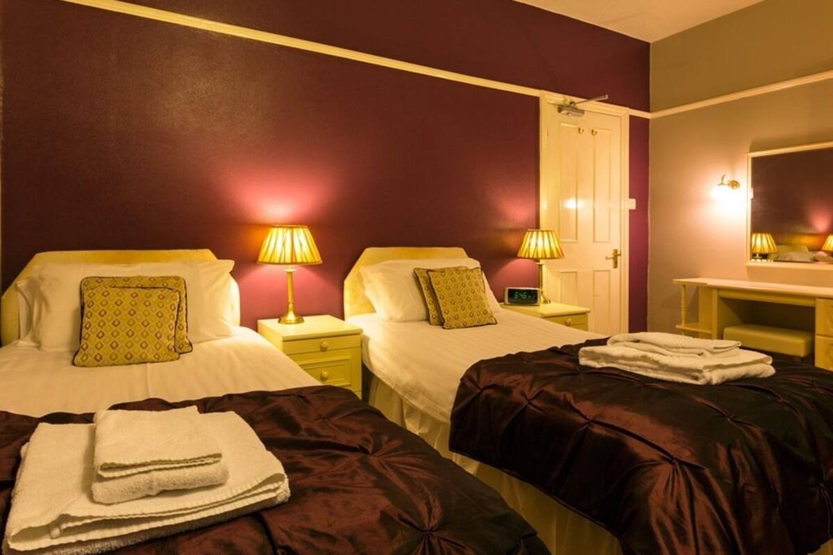 A hotel room with two beds, each with a pillow and a lamp. There is a desk with a chair and a mirror.