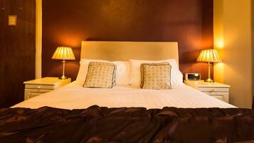 Una camera d'albergo con un letto grande, due abat-jour e una coperta scura.