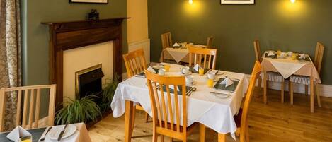 A dining area with wooden chairs and tables, a fireplace, and framed pictures on the walls.