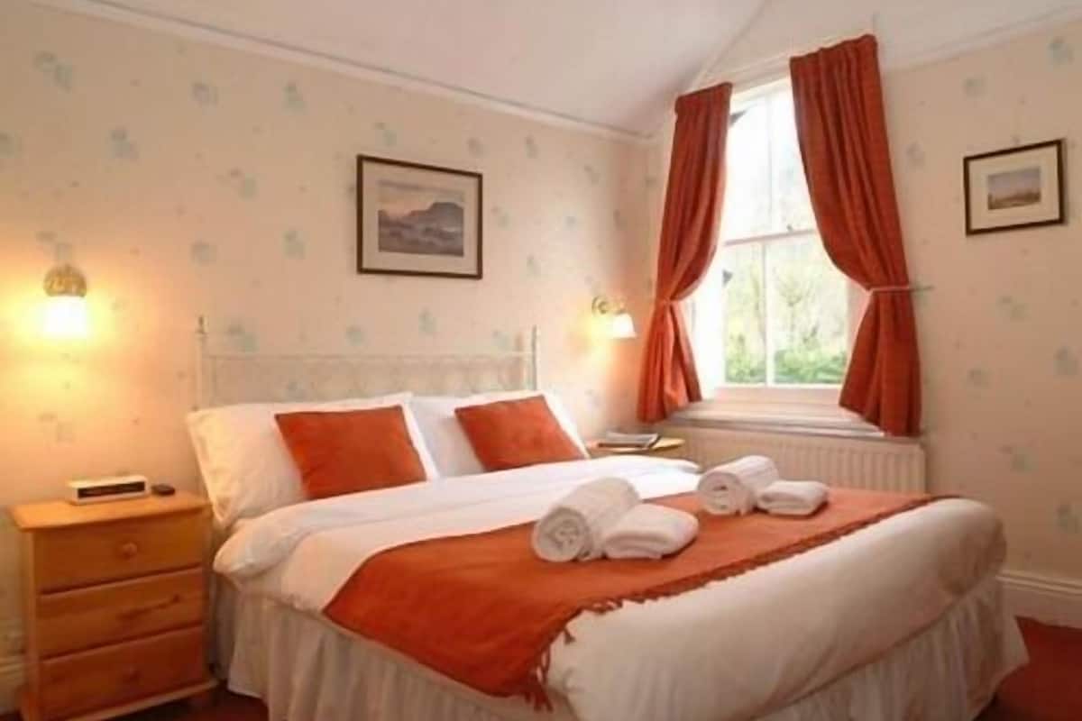 A bedroom with a bed, a nightstand, a dresser, and a window with curtains.
