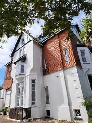 A two-story building with a white facade and red brick accents, featuring multiple windows and a small balcony.