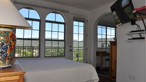 A bedroom with a large bed, a TV mounted on the wall, and a view of the outdoors through arched windows. - The Penrose Bed and Breakfast (Sedona)