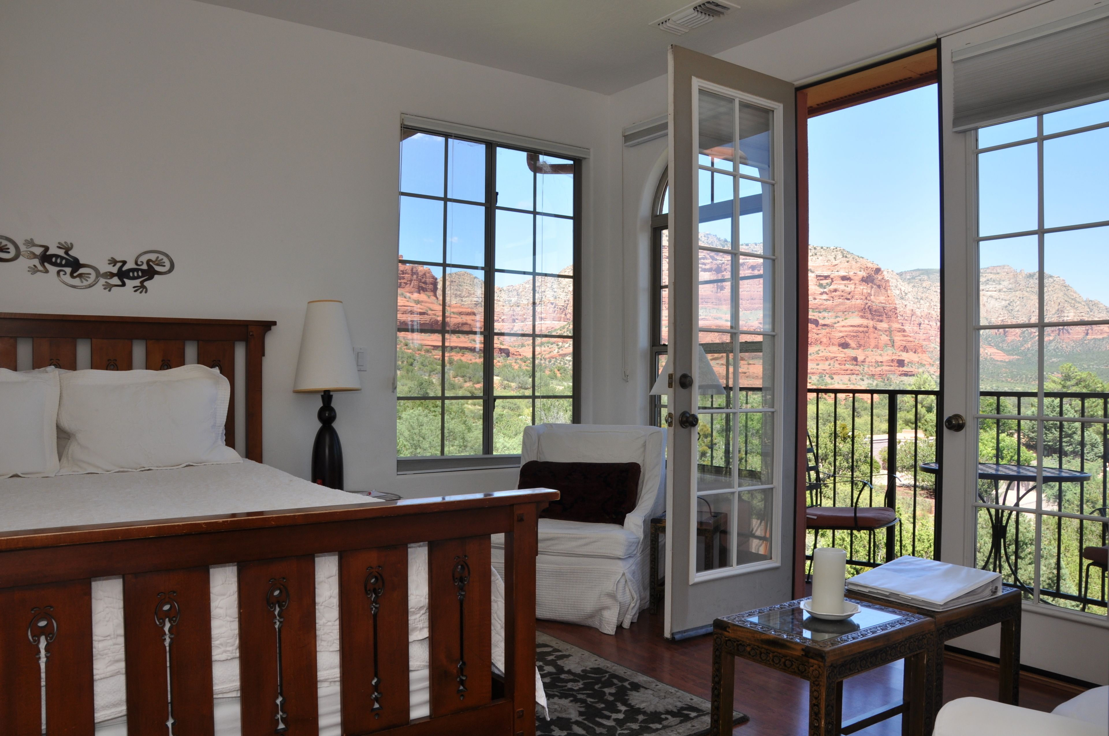 A bedroom with a wooden bed, a nightstand, a lamp, and a view of red rock formations through large windows.