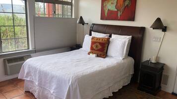Un lit bien fait, avec du linge de lit blanc, un tableau rouge et blanc au-dessus, et une petite table de chevet avec une lampe.