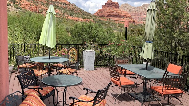 An outdoor patio with tables and chairs, surrounded by greenery and red rock formations in the background. - The Penrose Bed and Breakfast (Sedona)