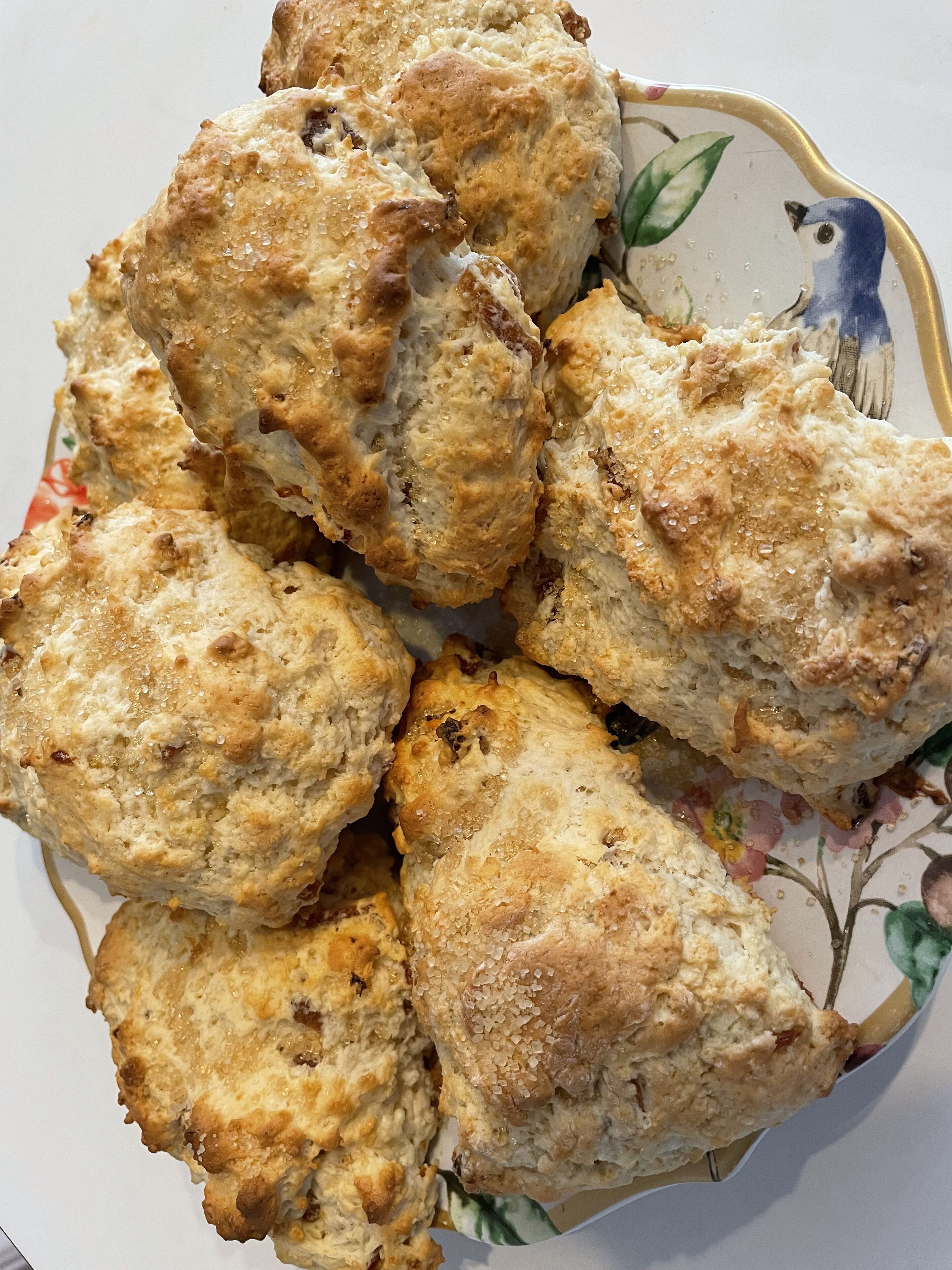 Ein Teller frisch gebackene Scones mit goldbrauner Kruste, serviert auf einem Teller mit Blumenmuster.