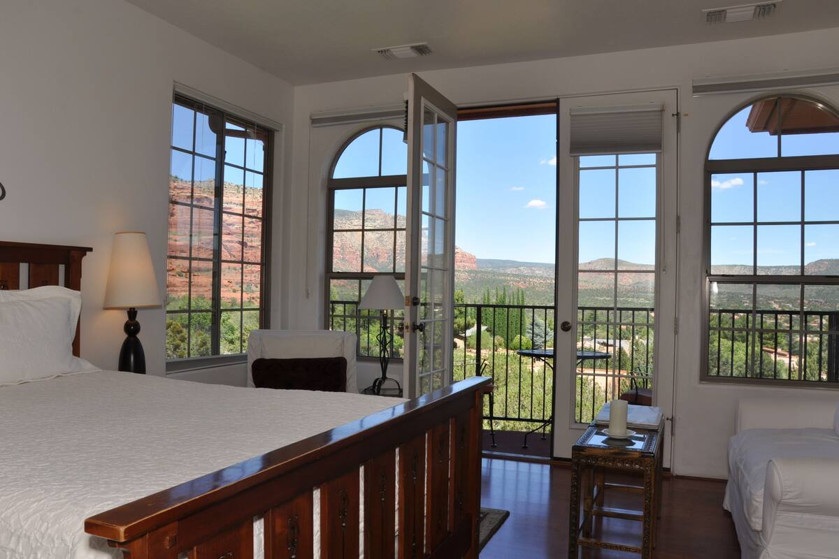 A bedroom with a large bed, a desk, and a balcony with a view of red rock formations.