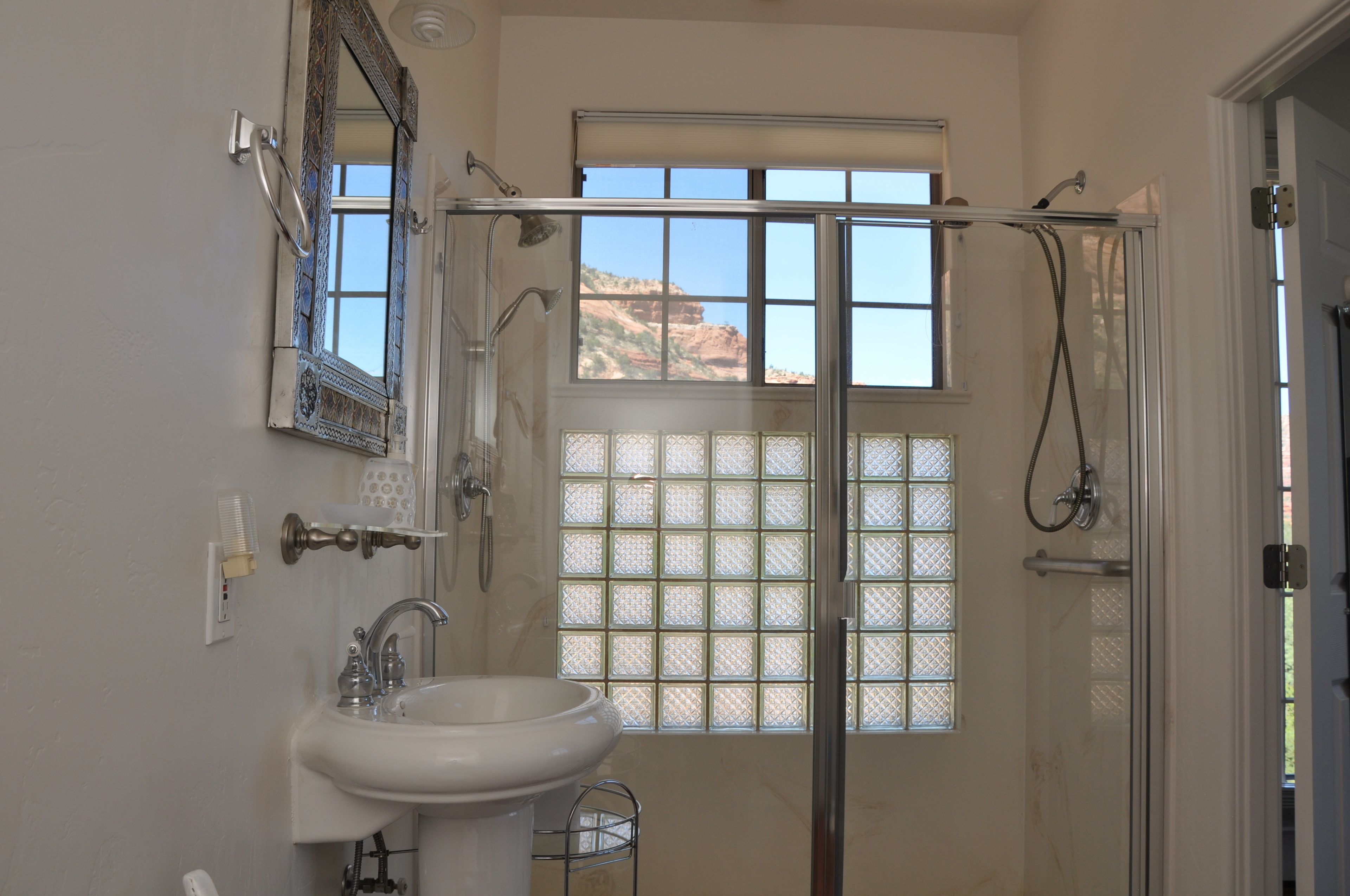 Un baño con ducha, lavamanos, espejo y ventana con vista a la montaña.