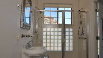 Un baño con ducha, lavamanos, espejo y ventana con vista a la montaña.