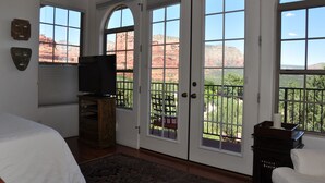 A bedroom with a large bed, a television on a wooden stand, and a view of red rock formations through the windows. - The Penrose Bed and Breakfast (Sedona)