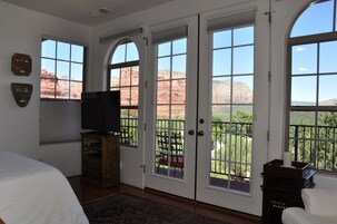 Un dormitorio con una cama grande, un televisor sobre un soporte de madera, y vistas a formaciones rocosas rojas a través de las ventanas.