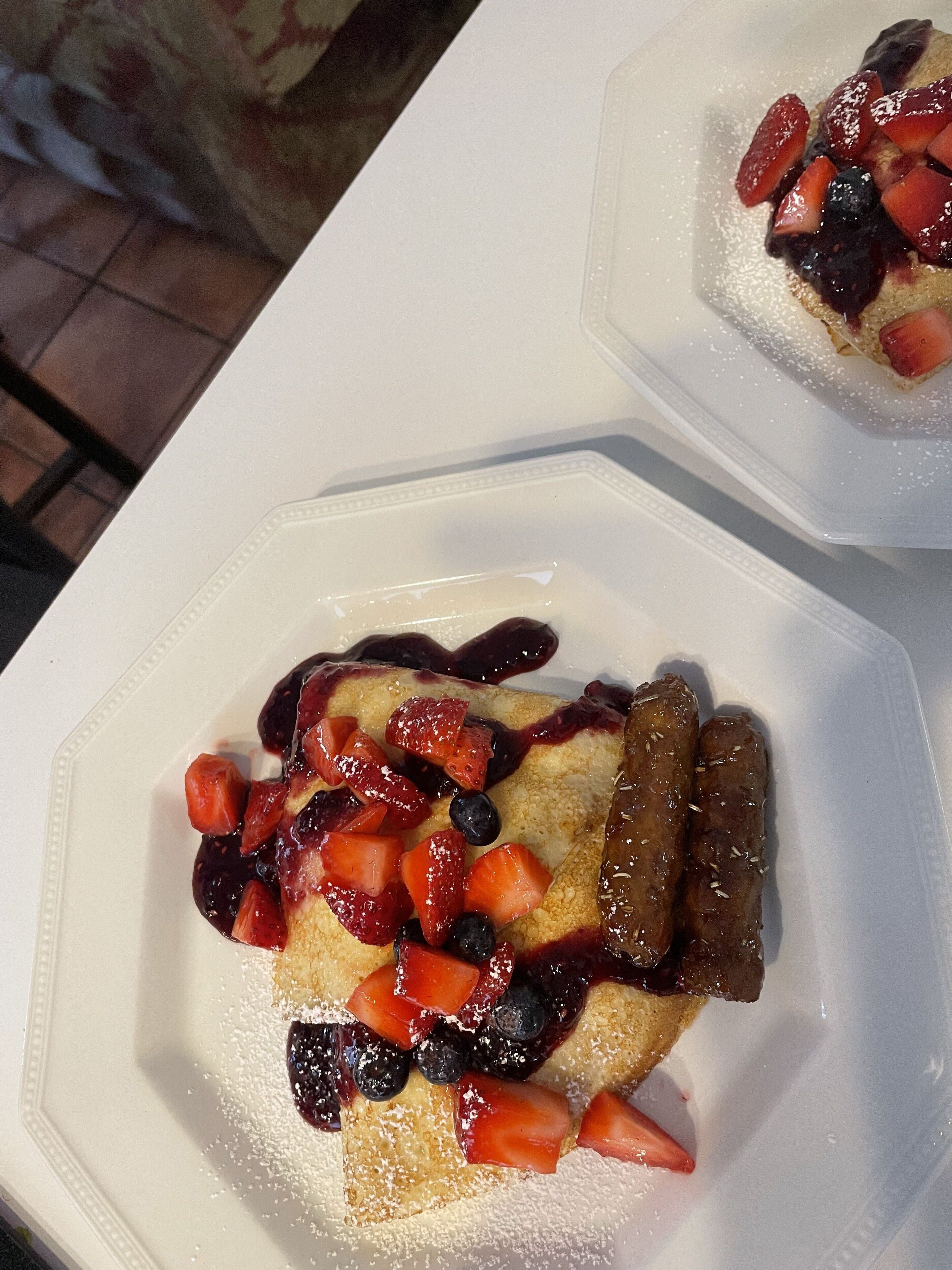 Une assiette de crêpes garnies de fraises, de myrtilles et nappées de sirop.