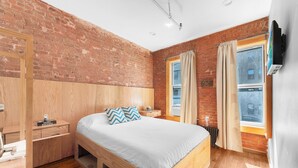 Une chambre avec un mur en briques, un cadre de lit en bois, une table de chevet, une commode et une fenêtre avec des rideaux.