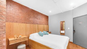 Une chambre moderne avec un mur en briques, une tête de lit en bois et un lit recouvert de linge de lit blanc.