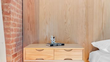 Un dormitorio pequeño y acogedor con una mesita de noche de madera, un taburete y una cama con ropa de cama blanca.