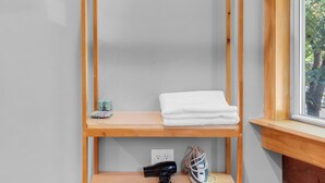 Une étagère en bois avec un miroir, une serviette pliée et un appareil photo sur l’étagère inférieure.