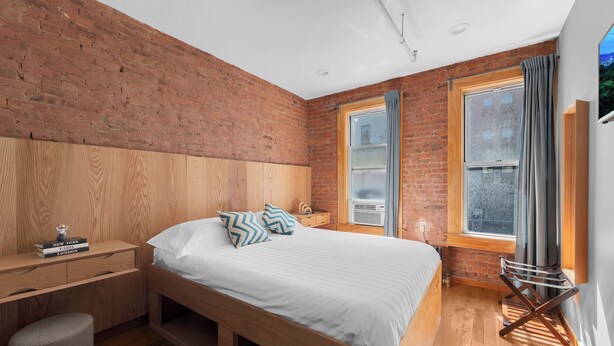 Une chambre à coucher avec un lit en bois, une table de chevet, un bureau et une fenêtre avec des rideaux.