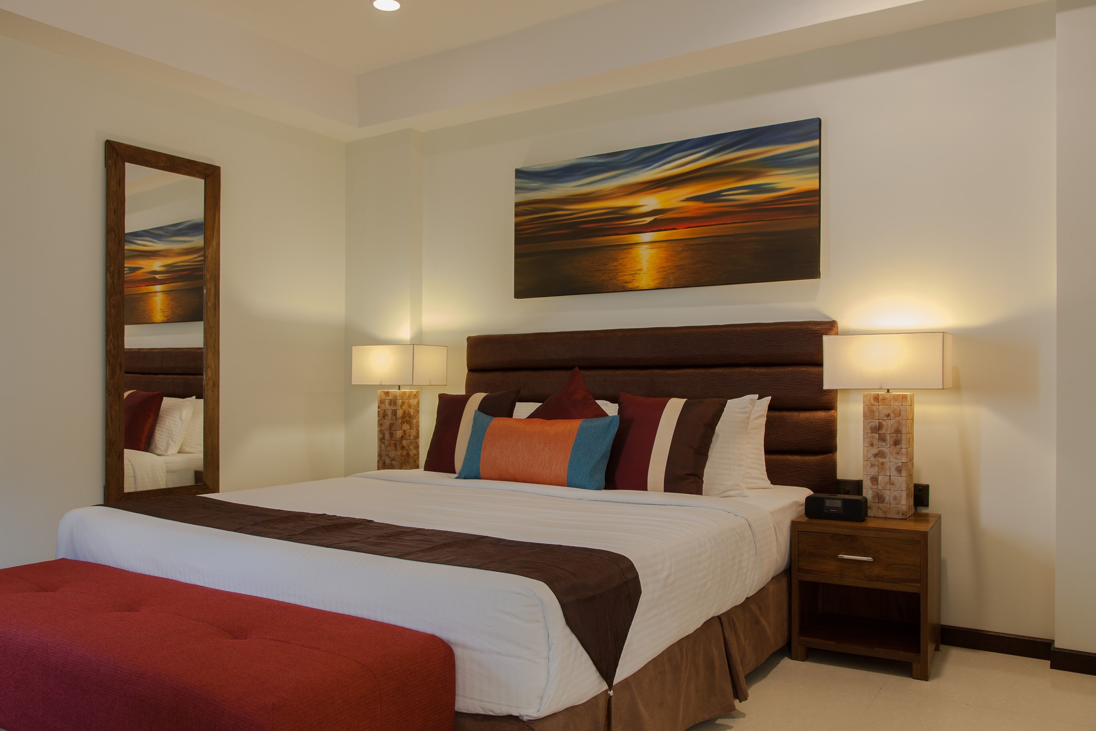 A neatly arranged hotel room with a large bed, two bedside tables with lamps, a mirror, and a painting on the wall.