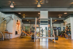 Une salle de sport équipée de divers appareils d’exercice, dotée d’un plancher en bois et d’un miroir sur un des murs.