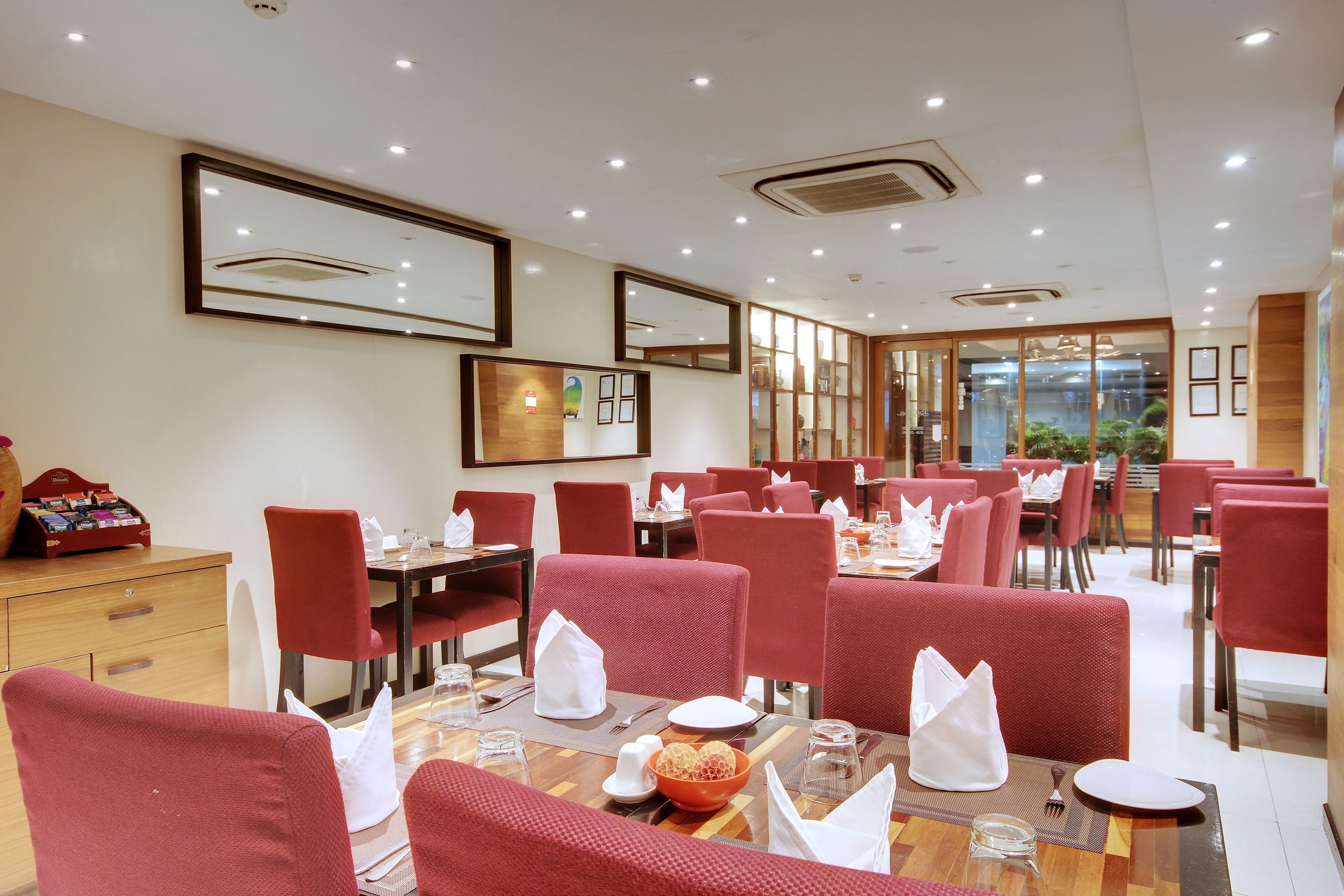 A hotel dining area with red upholstered chairs, wooden tables, and white table settings.
