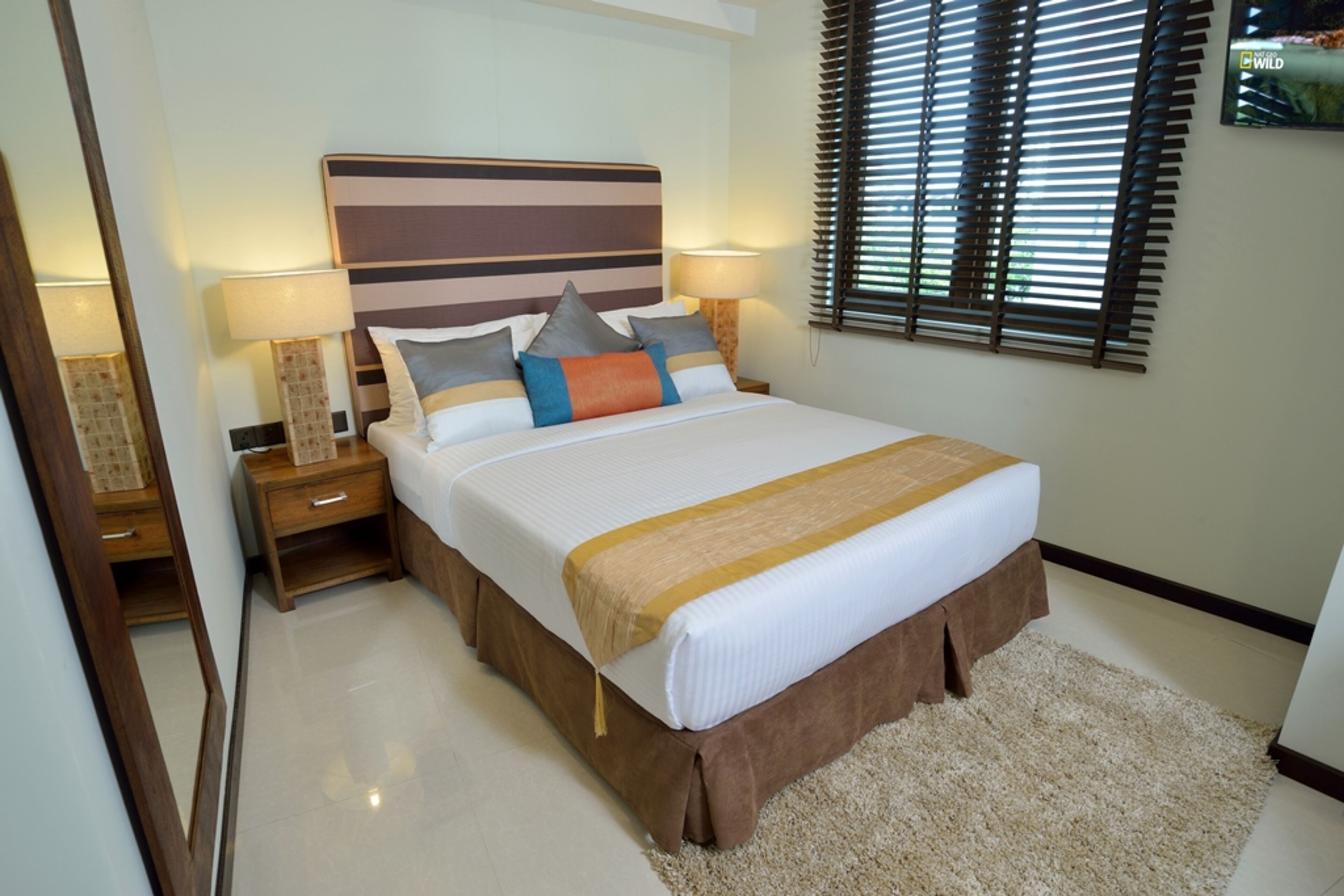 A neatly arranged bedroom with a large bed, two bedside tables, and a wall-mounted TV.