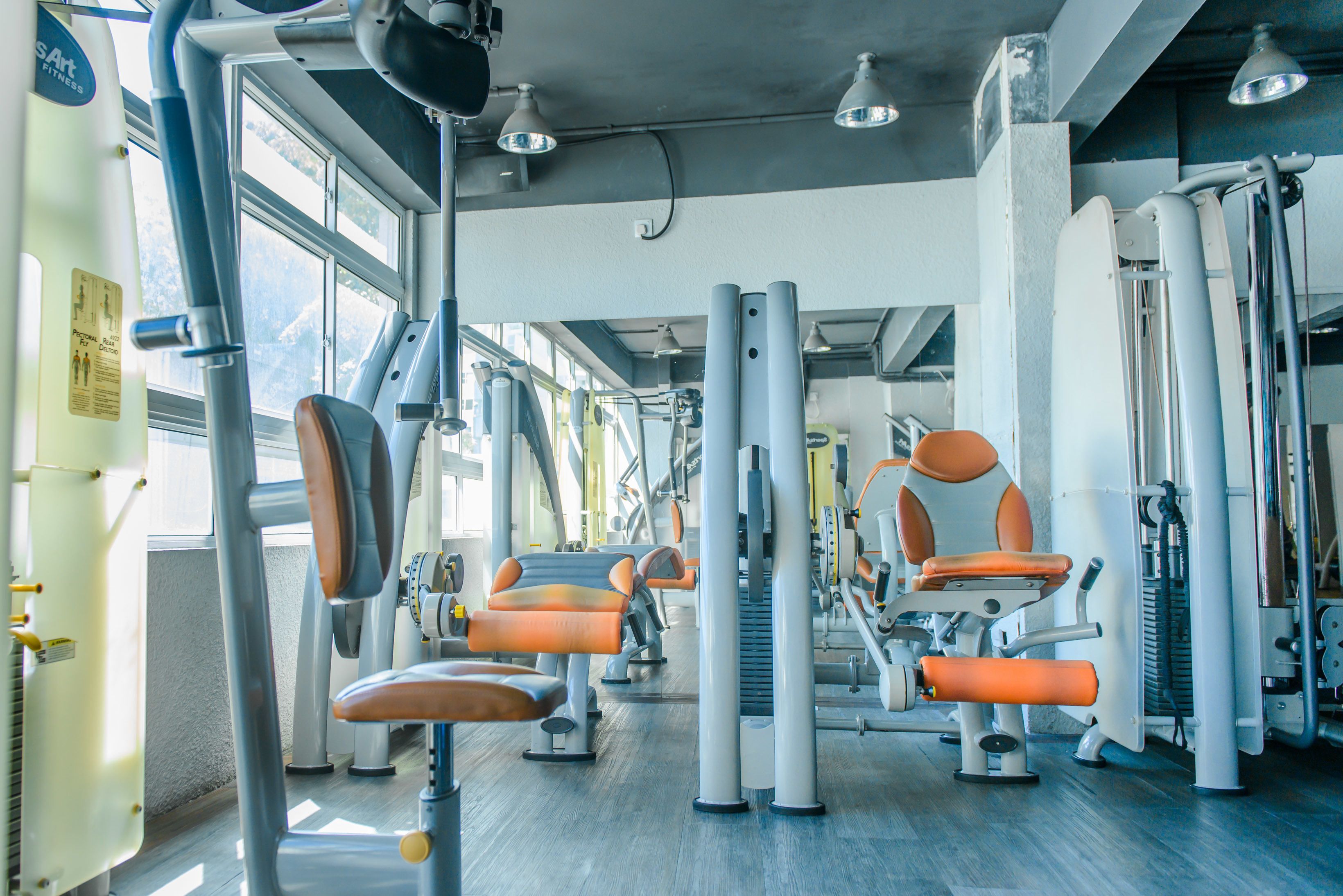 A gym with exercise equipment, large windows, and a wooden floor.