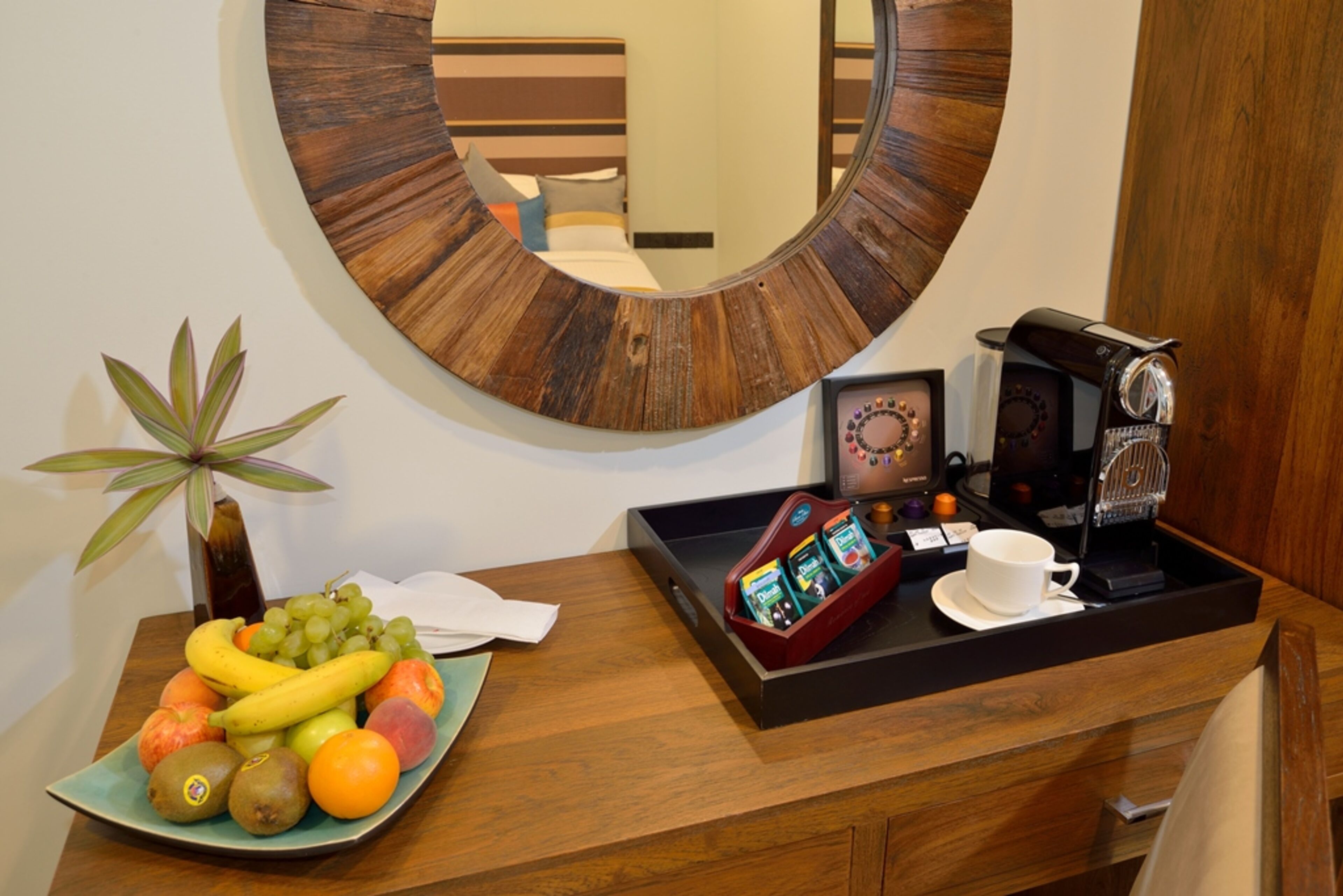 Une chambre d’hôtel avec une table de chevet en bois, une assiette de fruits, une machine à café et un miroir.