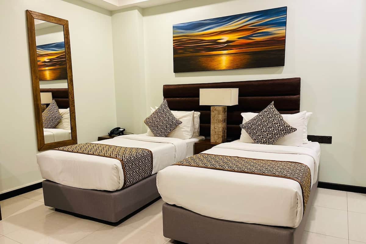 A hotel room with two beds, a large mirror, a painting, and a bedside lamp.