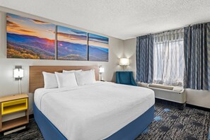 A hotel room with a large bed, two wall-mounted lamps, a nightstand, a window with curtains, and a wall with three landscape paintings. - Days Inn by Wyndham Chattanooga/Hamilton Place (Chattanooga)