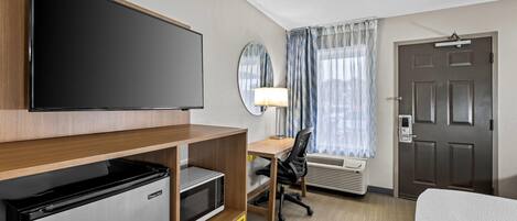 Habitación de hotel con televisión de pantalla plana, microondas, escritorio con silla, cama, ventana con cortinas y puerta con picaporte.
