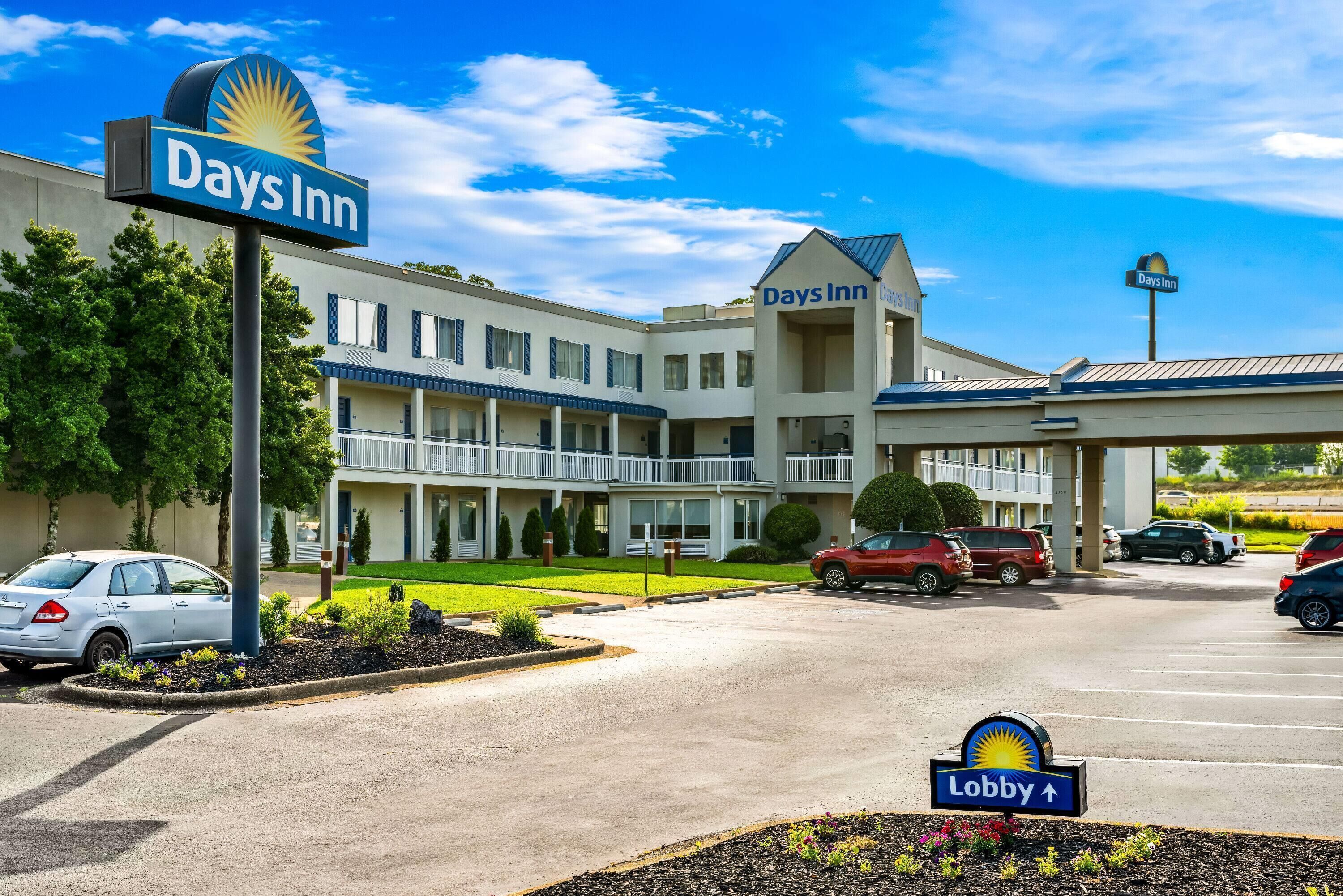 A Days Inn hotel with a visible lobby sign, multiple-story building, and a parking lot with several cars.