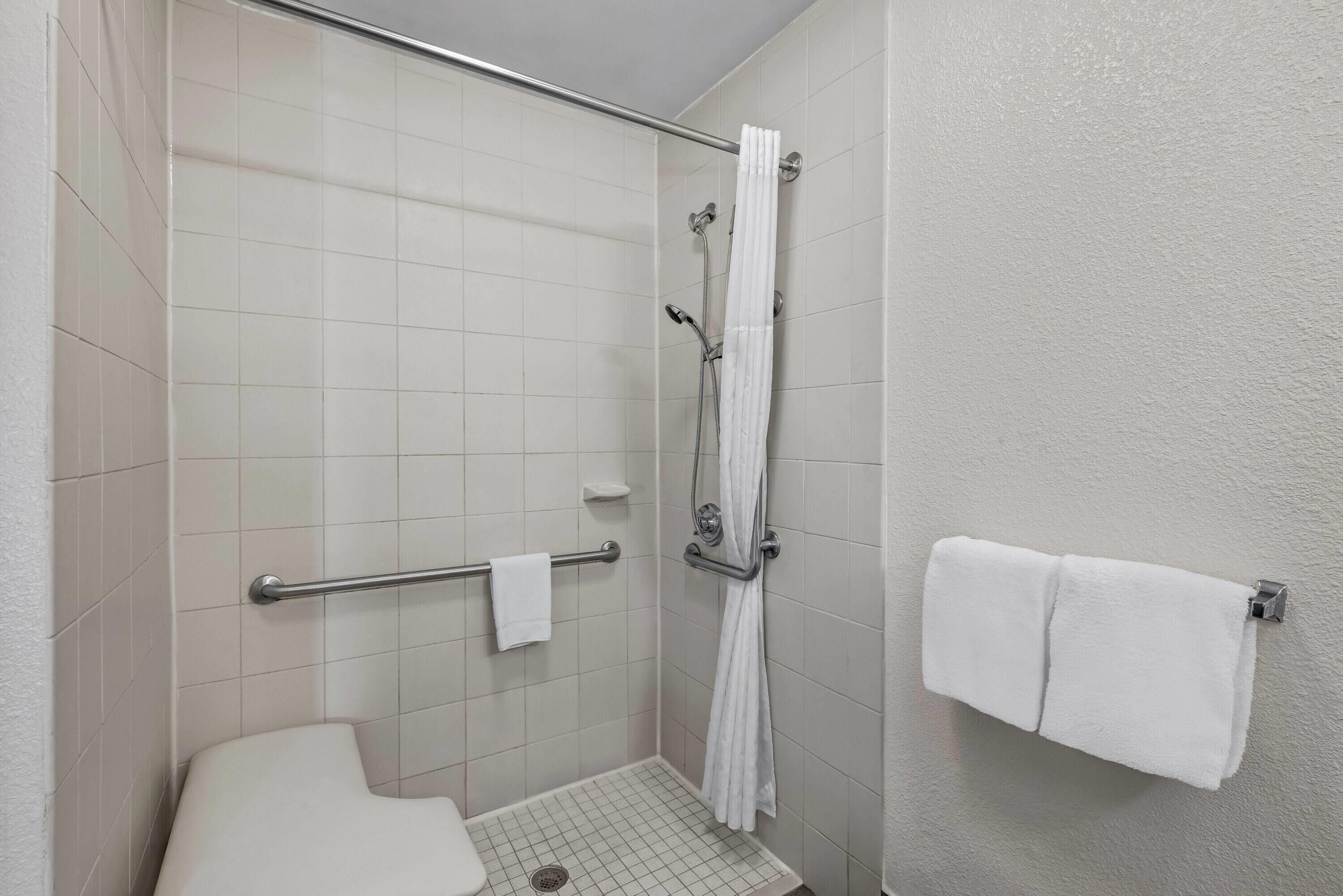 A small, enclosed shower area with a grab bar, a white toilet, and a towel rack.