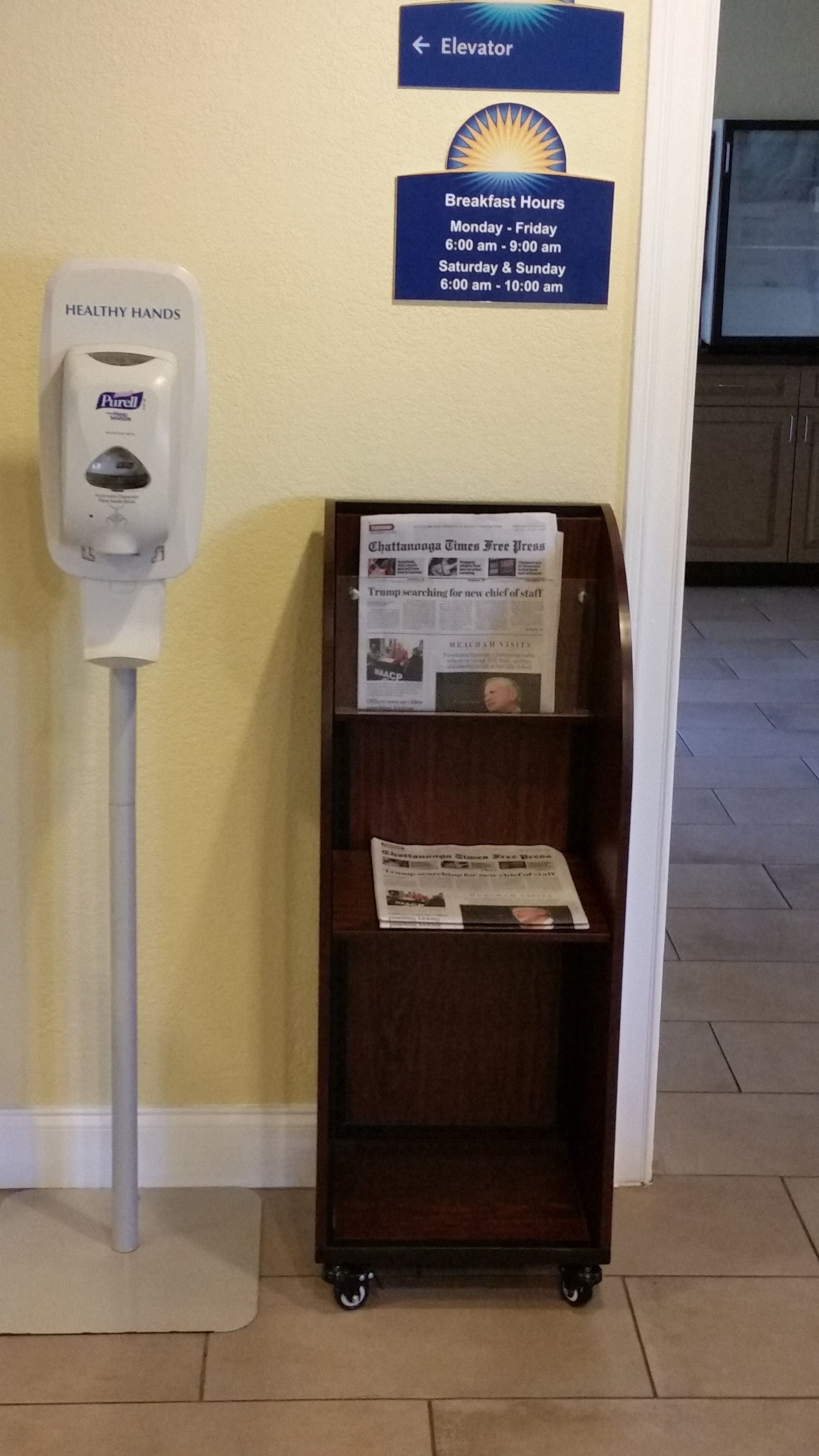 Een handdesinfecteerder, een bord met de ontbijttijden, en een krantenrek met een 'Chattanooga Times Free Press' krant.