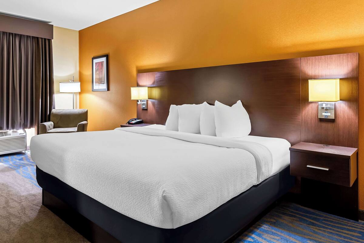 A hotel room with a large bed, a bedside table, a lamp, and a chair.