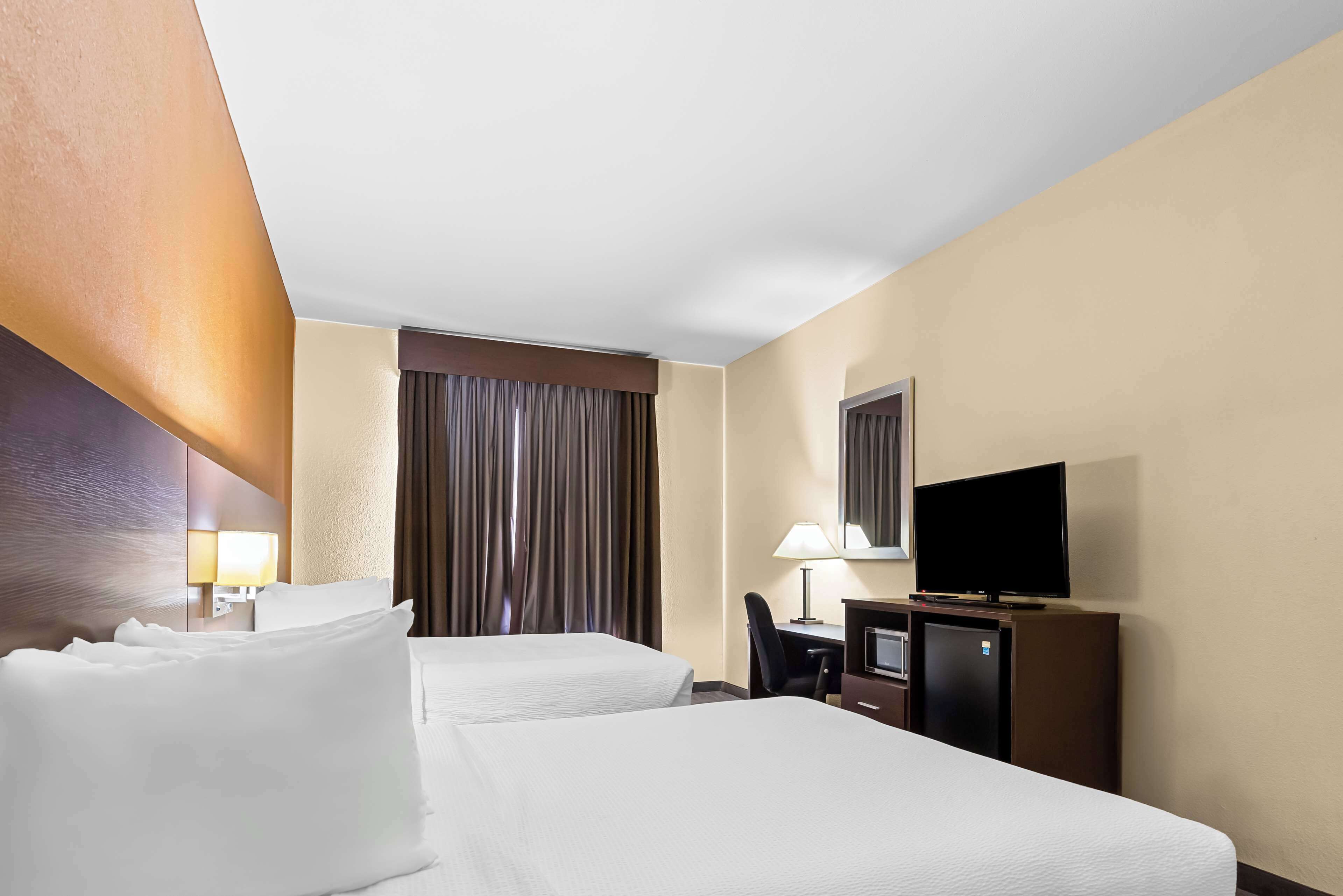 A hotel room with two beds, a desk, a television, and a minibar.