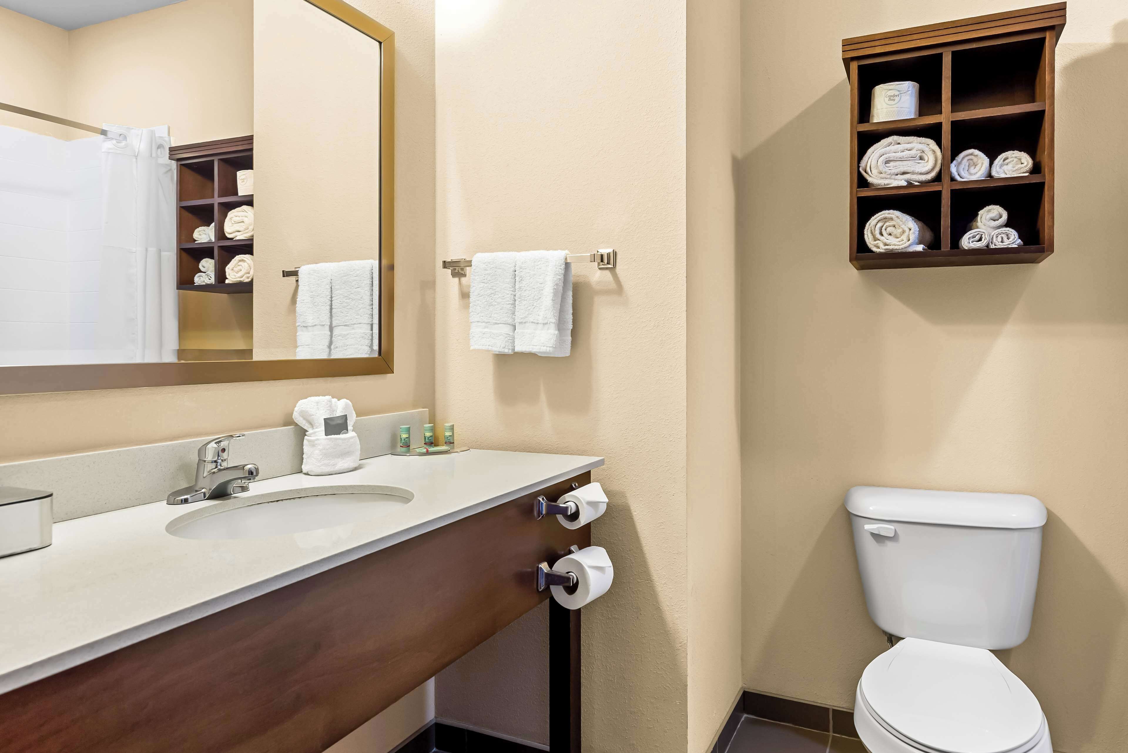 A bathroom with a sink, mirror, towel rack, toilet, and a shelf with towels.
