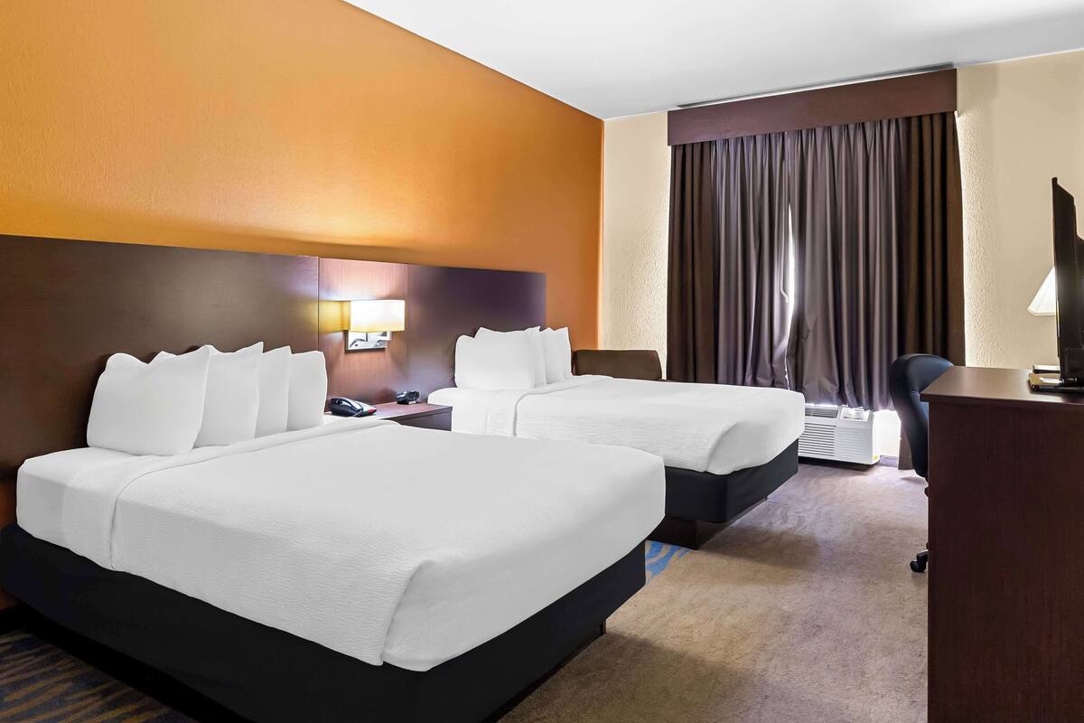 A hotel room with two beds, a desk, a chair, a TV, and a window with curtains.