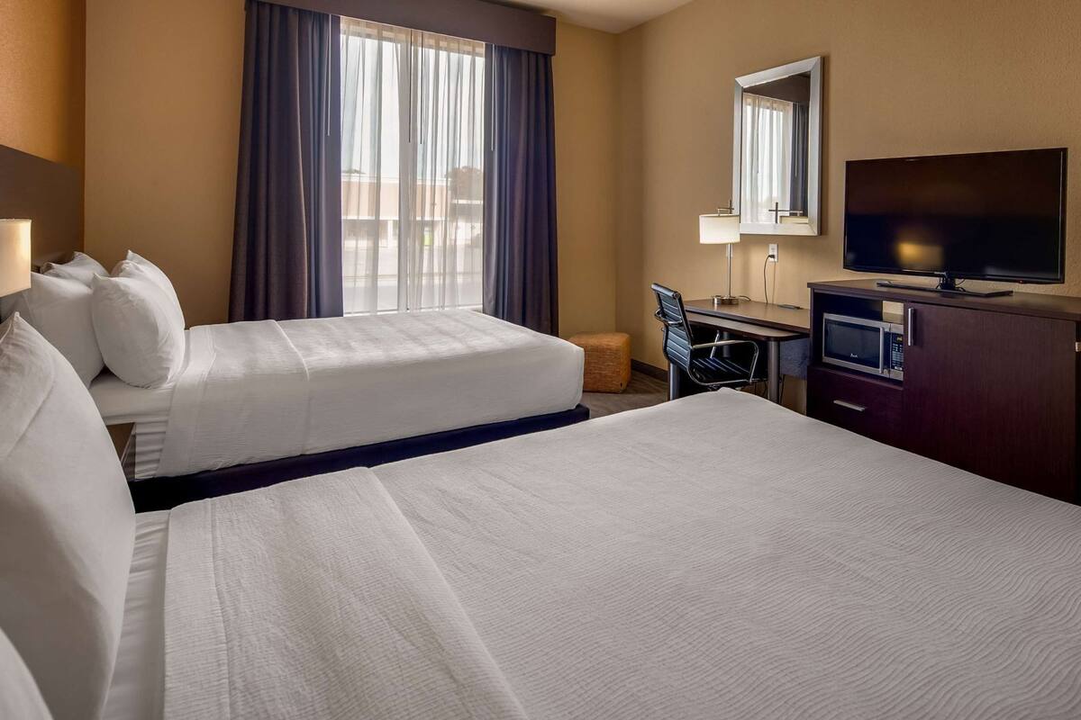 A hotel room with two beds, a desk, a television, and a microwave.